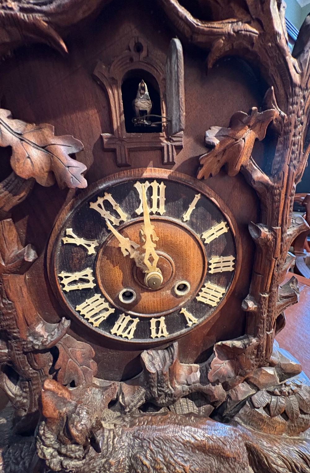 An intricately hand-carved dark wood Black Forest cuckoo clock featuring a bird atop a nest, a framed dial with Roman numerals, and a fox figure at the base. View VIII