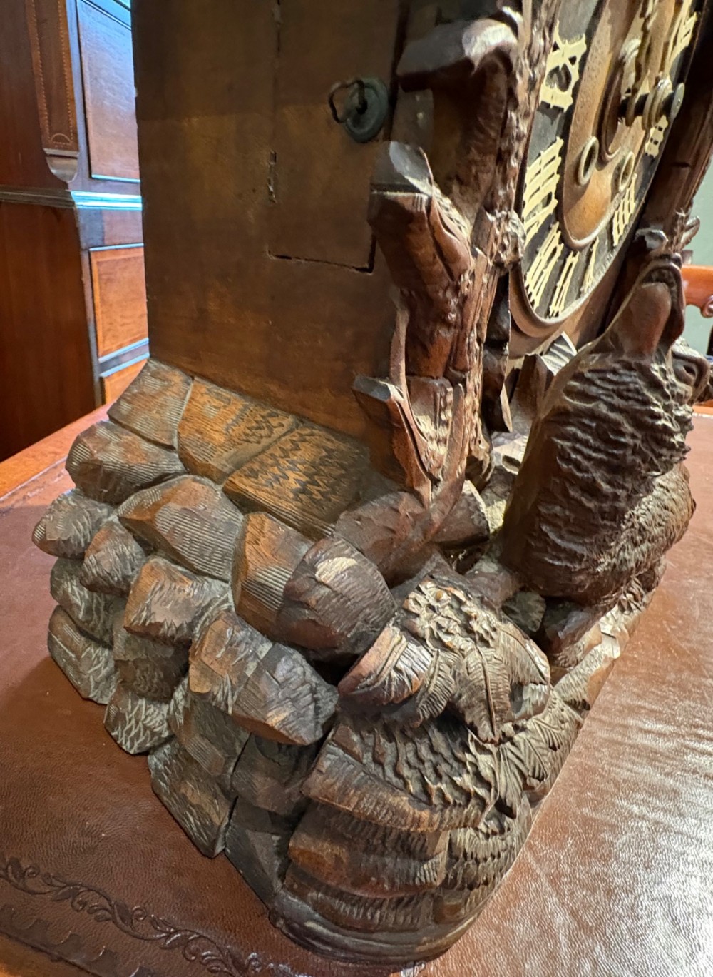 An intricately hand-carved dark wood Black Forest cuckoo clock featuring a bird atop a nest, a framed dial with Roman numerals, and a fox figure at the base. View X