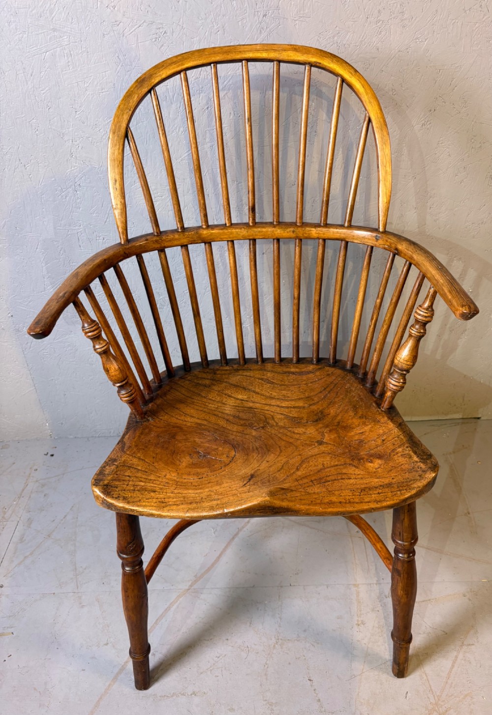An antique Georgian fruitwood Windsor armchair featuring a arched stick back, turned arm supports, and a contoured solid wood saddle seat.