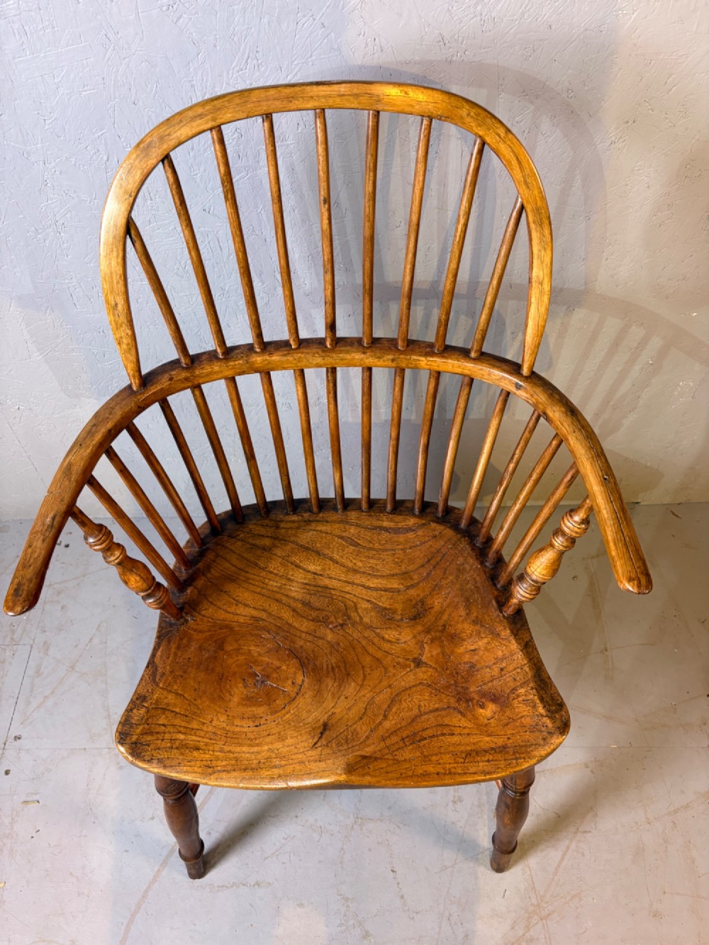 An antique Georgian fruitwood Windsor armchair featuring a arched stick back, turned arm supports, and a contoured solid wood saddle seat. View II