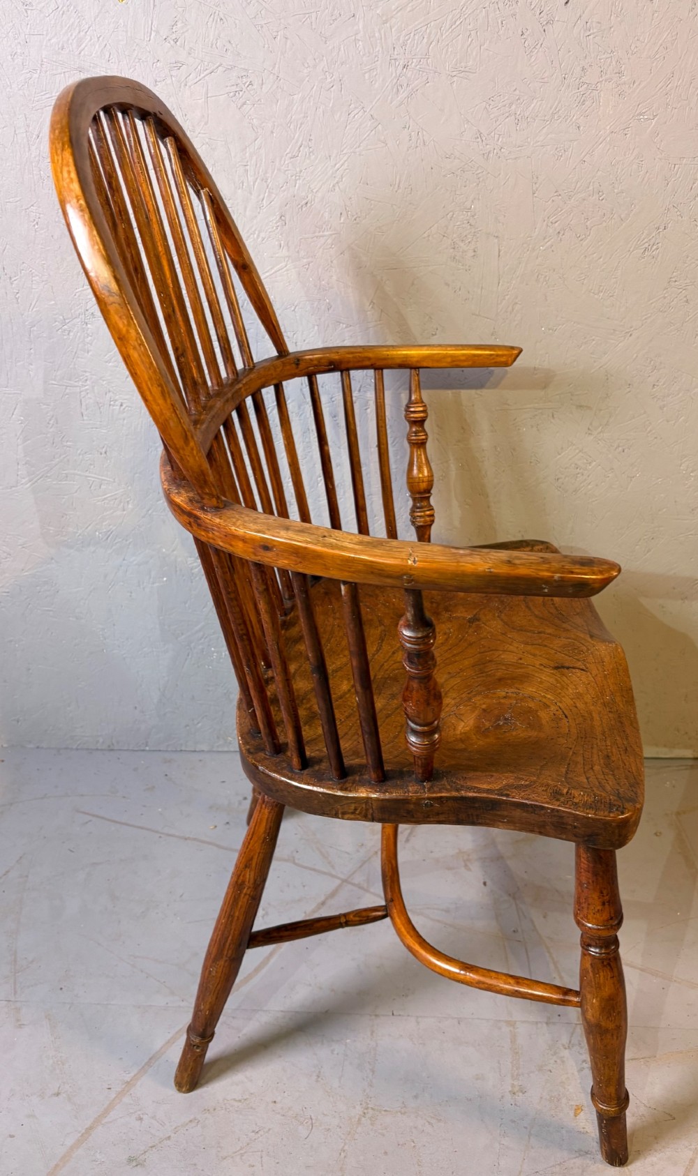 An antique Georgian fruitwood Windsor armchair featuring a arched stick back, turned arm supports, and a contoured solid wood saddle seat. View III