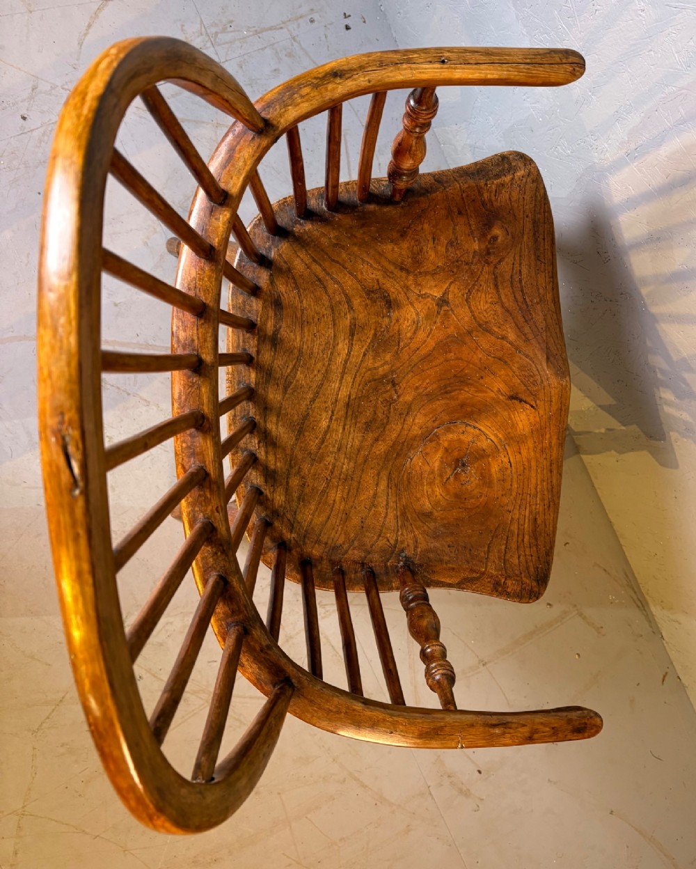 An antique Georgian fruitwood Windsor armchair featuring a arched stick back, turned arm supports, and a contoured solid wood saddle seat. View V