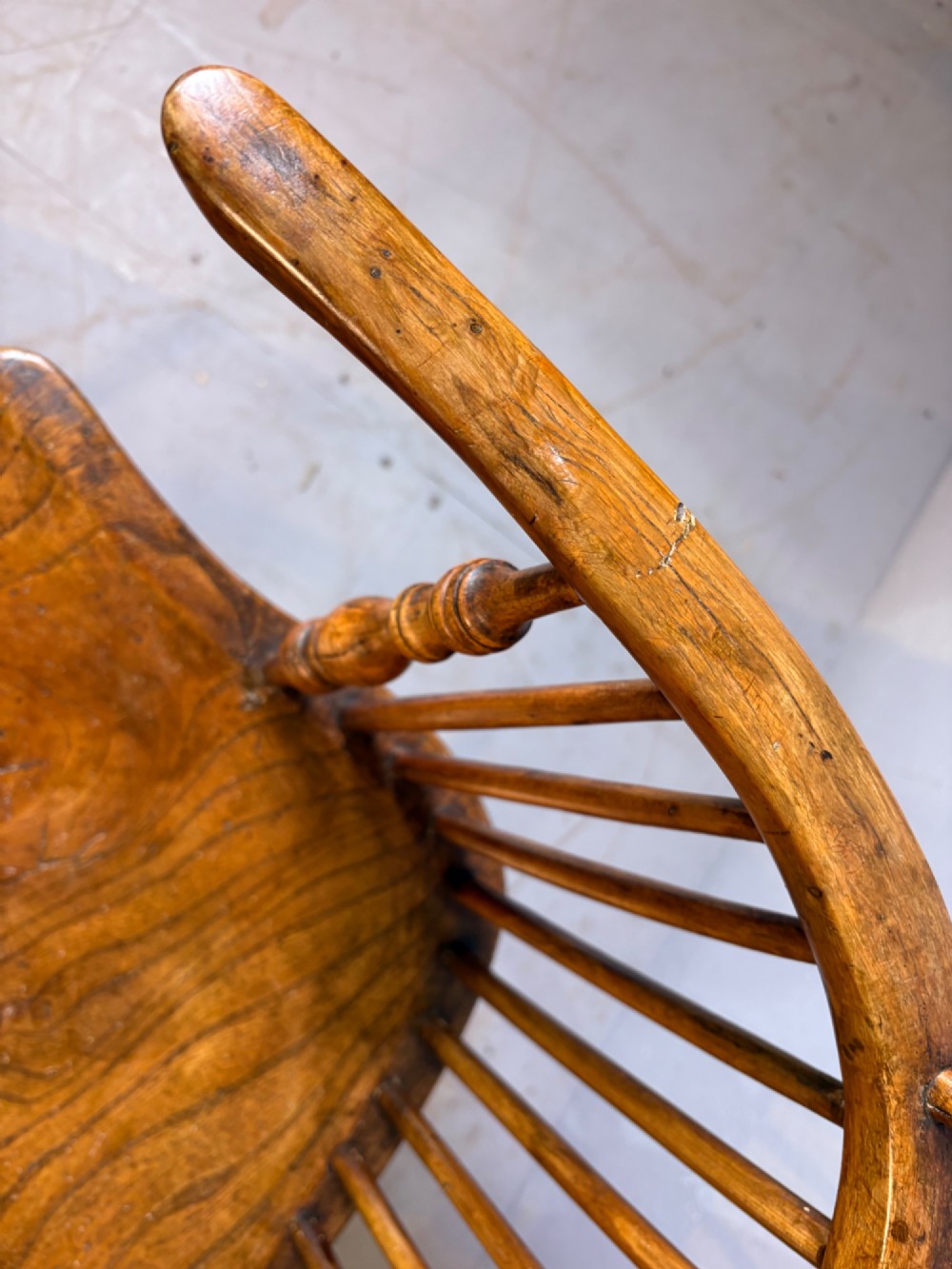 An antique Georgian fruitwood Windsor armchair featuring a arched stick back, turned arm supports, and a contoured solid wood saddle seat. View VII