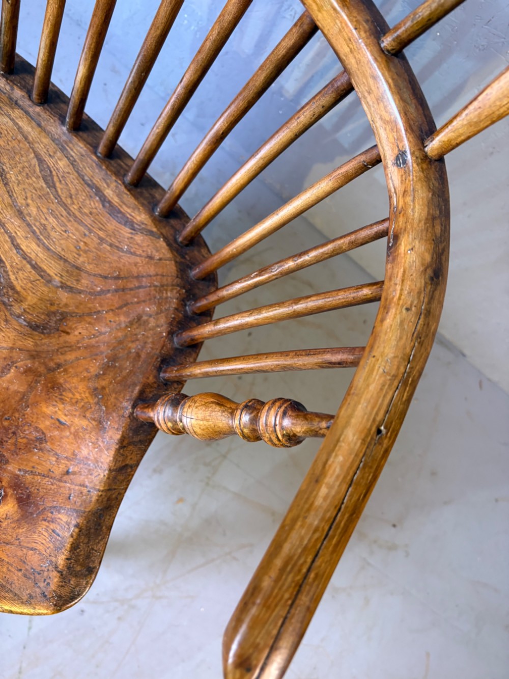 An antique Georgian fruitwood Windsor armchair featuring a arched stick back, turned arm supports, and a contoured solid wood saddle seat. View VIII