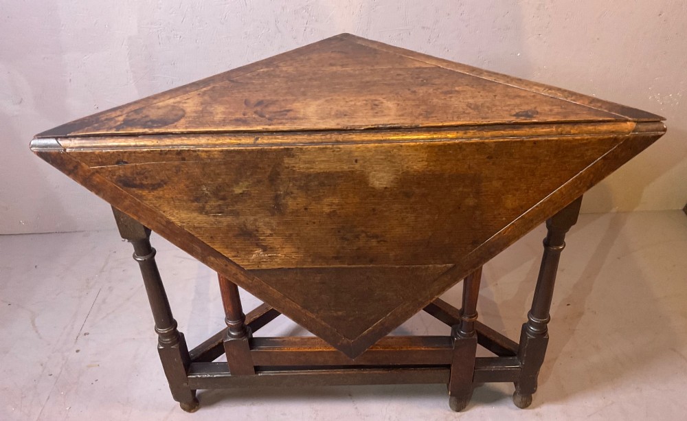 A 17th-century oak credence table featuring a triangular folding top resting on a framework with turned legs and low stretchers.