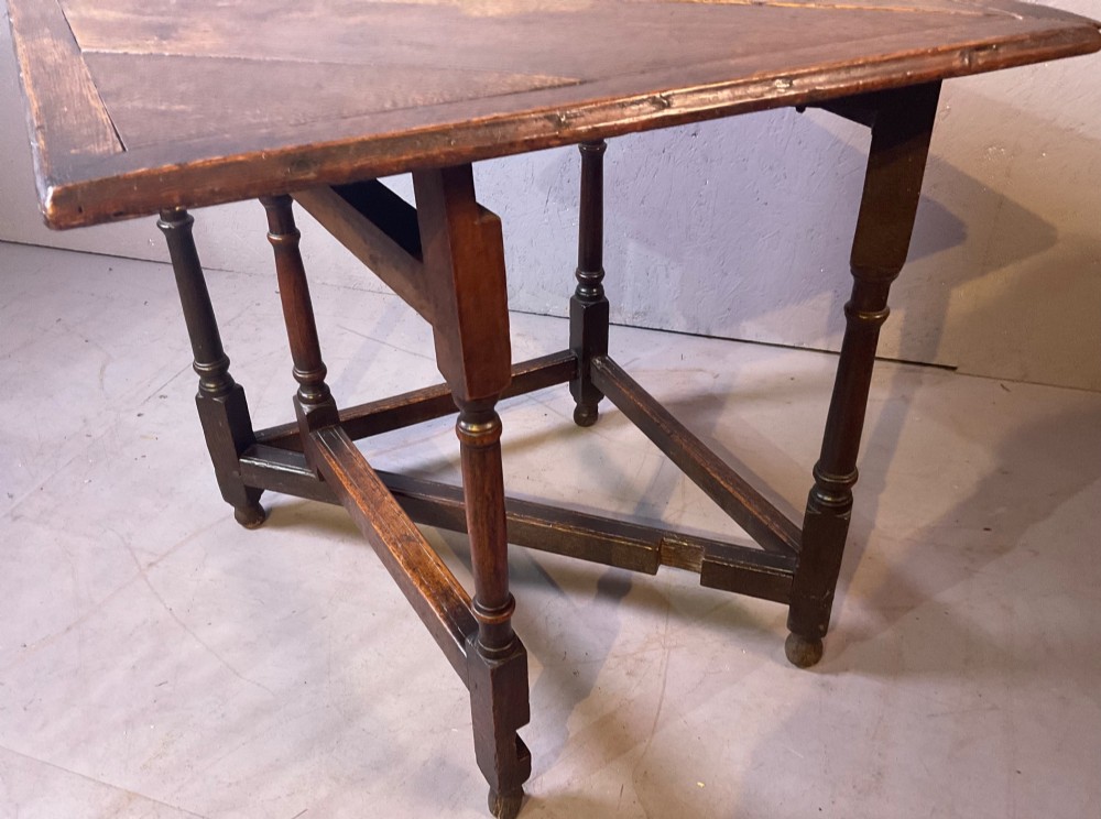 A 17th-century oak credence table featuring a triangular folding top resting on a framework with turned legs and low stretchers. View V