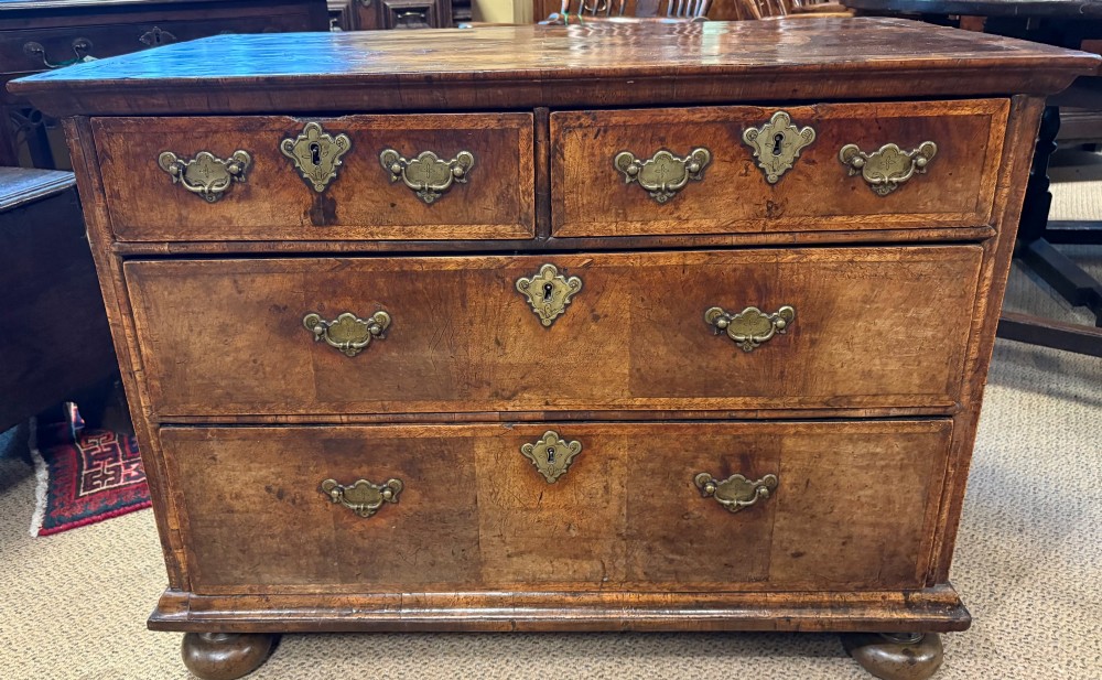An early eighteenth-century walnut chest of drawers featuring two short drawers over two long drawers with brass drop handles and turned bun feet.