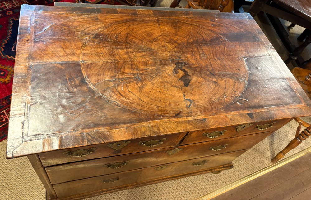 An early eighteenth-century walnut chest of drawers featuring two short drawers over two long drawers with brass drop handles and turned bun feet. View VI