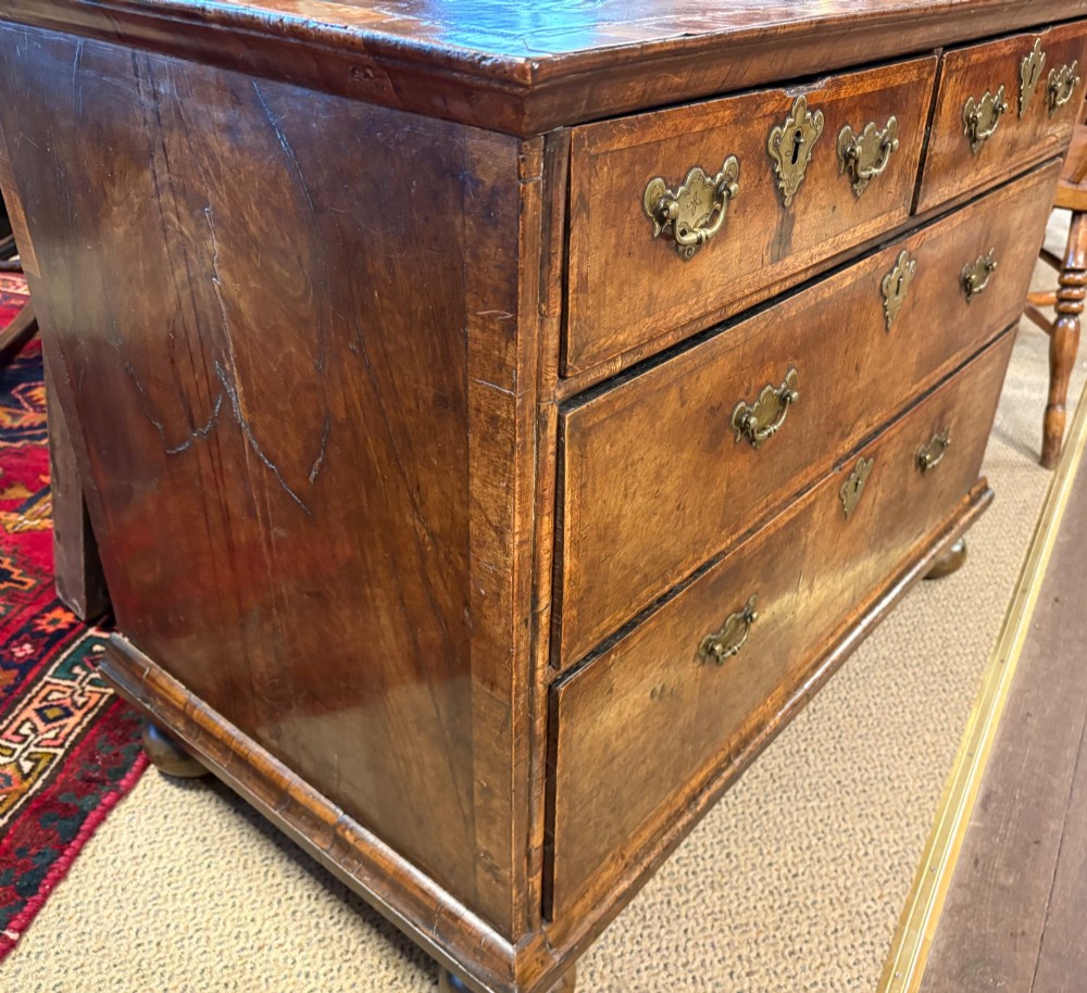 An early eighteenth-century walnut chest of drawers featuring two short drawers over two long drawers with brass drop handles and turned bun feet. View XIII