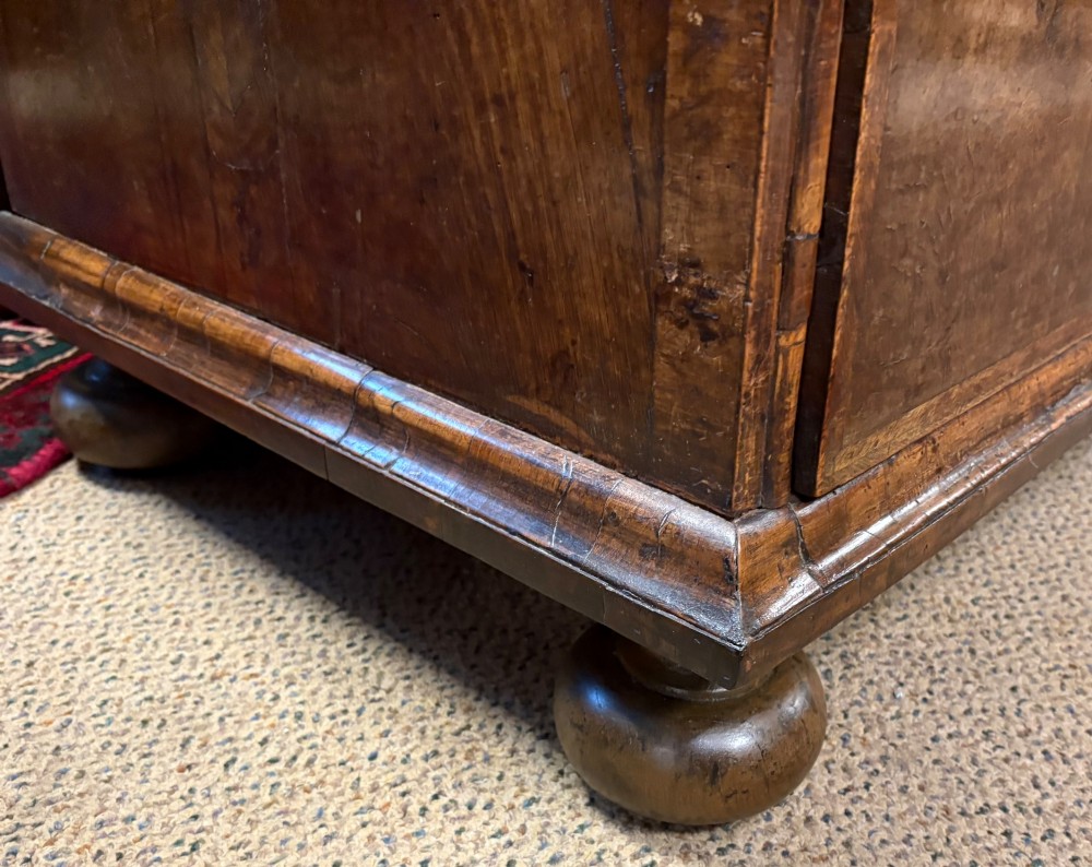 An early eighteenth-century walnut chest of drawers featuring two short drawers over two long drawers with brass drop handles and turned bun feet. View XIV
