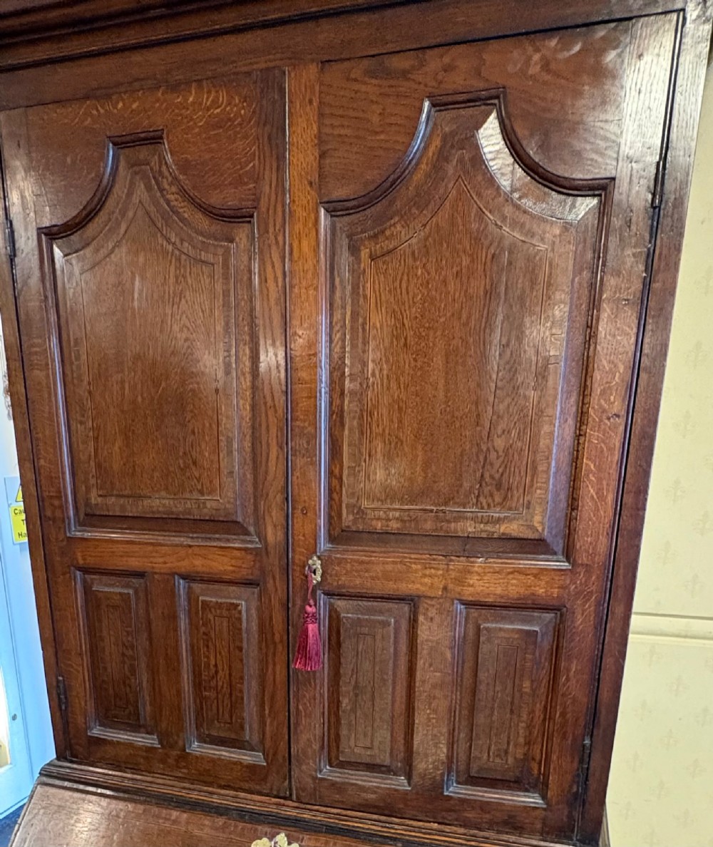 An 18th-century dark oak bureau bookcase featuring an upper cabinet with double panelled doors above a slant-front writing desk and lower drawers with brass handles. View II