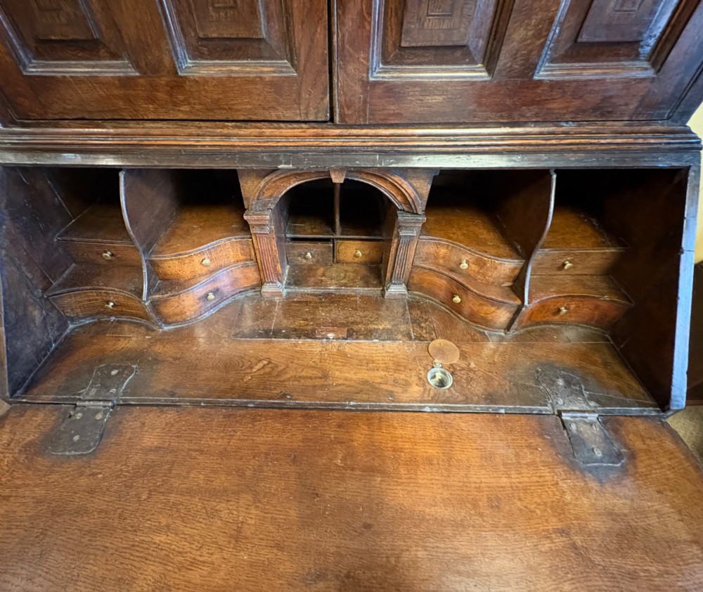 An 18th-century dark oak bureau bookcase featuring an upper cabinet with double panelled doors above a slant-front writing desk and lower drawers with brass handles. View V