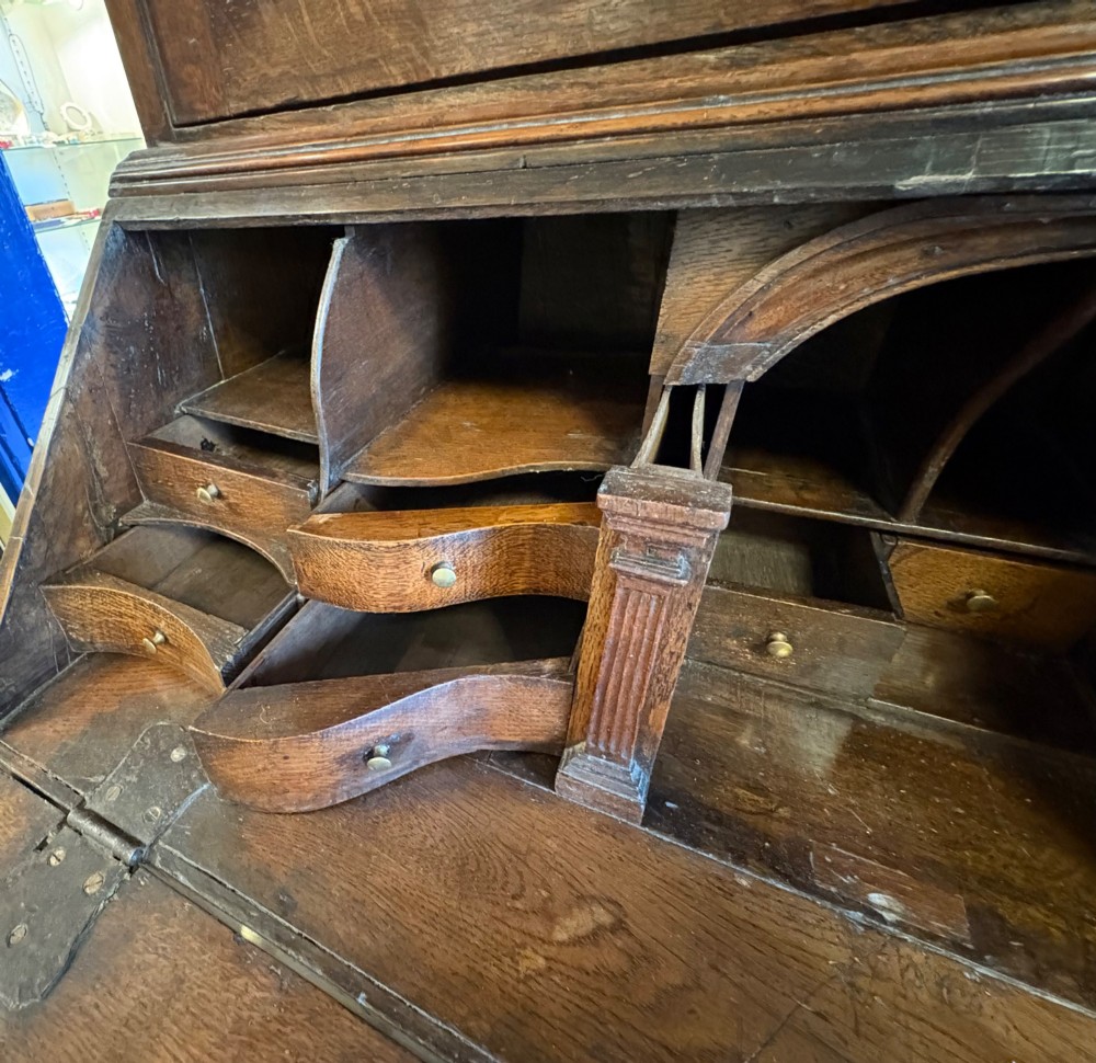 An 18th-century dark oak bureau bookcase featuring an upper cabinet with double panelled doors above a slant-front writing desk and lower drawers with brass handles. View VI