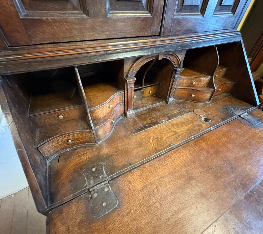 An 18th-century dark oak bureau bookcase featuring an upper cabinet with double panelled doors above a slant-front writing desk and lower drawers with brass handles. View VII
