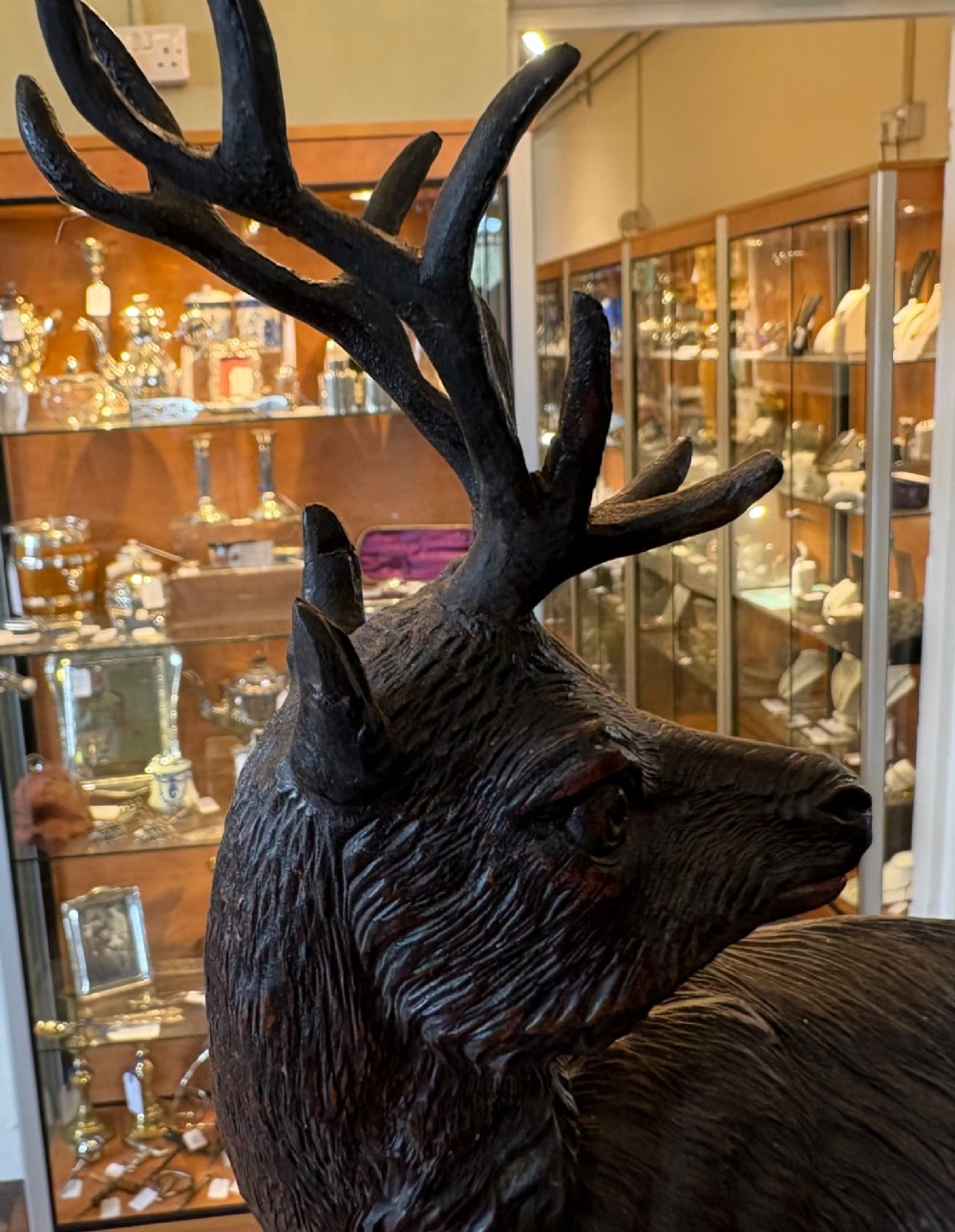 A dark hand-carved wooden Black Forest sculpture depicting two horned animals positioned on a craggy rocky outcrop beside a gnarled tree branch. View VII