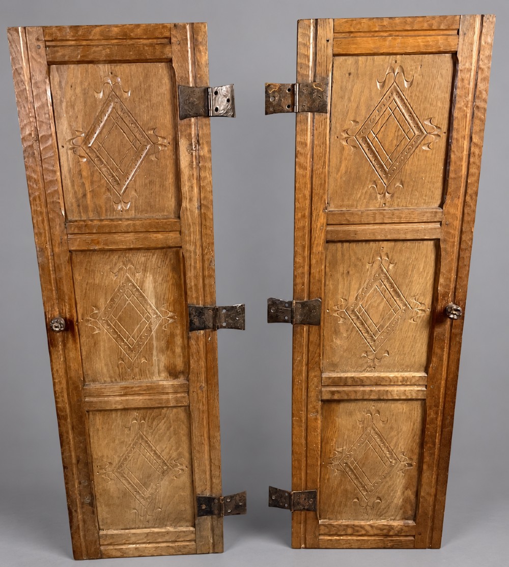 A pair of hand-adzed solid oak cabinet doors featuring three recessed panels with carved diamond motifs and iron strap hinges.