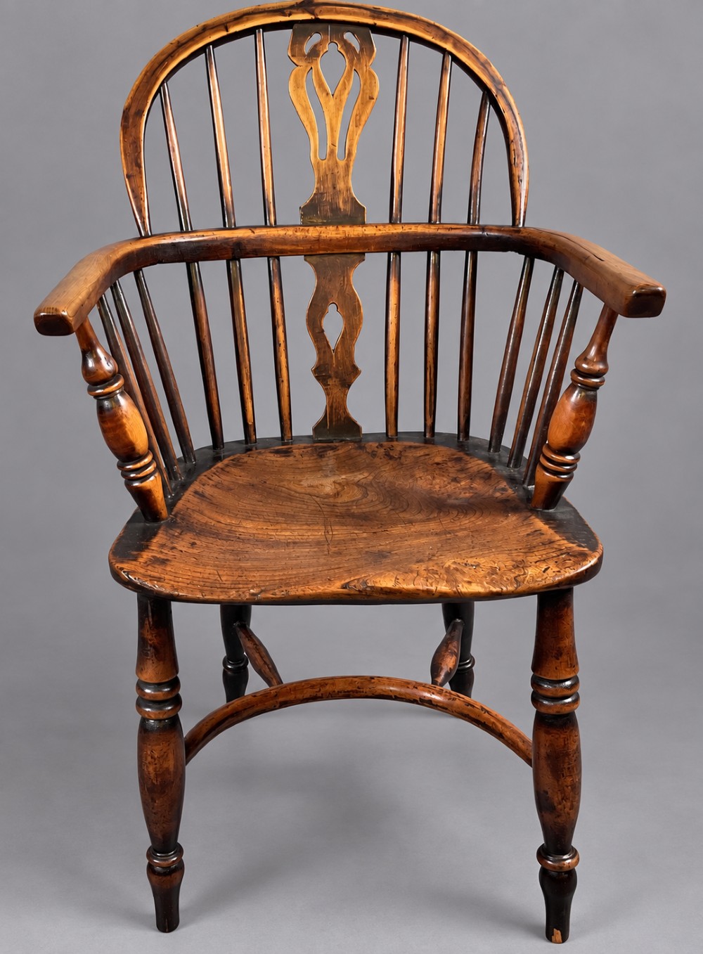 An antique yew wood low-back Windsor armchair featuring a pierced decorative back splat, turned legs, a shaped wooden seat, and a curved crinoline stretcher.