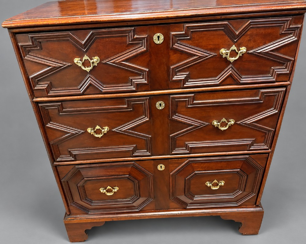 An 18th-century mahogany chest of drawers featuring geometric mitred mouldings, cast brass swan-neck handles, keyhole escutcheons, and bracket feet.