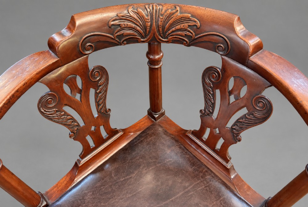 An 18th century Georgian mahogany corner chair featuring carved back splats, scrolled arms, a dark leather seat, and cabriole legs with ball and claw feet. View II