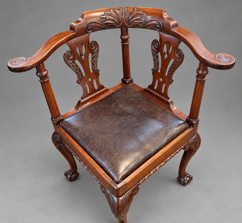 An 18th century Georgian mahogany corner chair featuring carved back splats, scrolled arms, a dark leather seat, and cabriole legs with ball and claw feet.