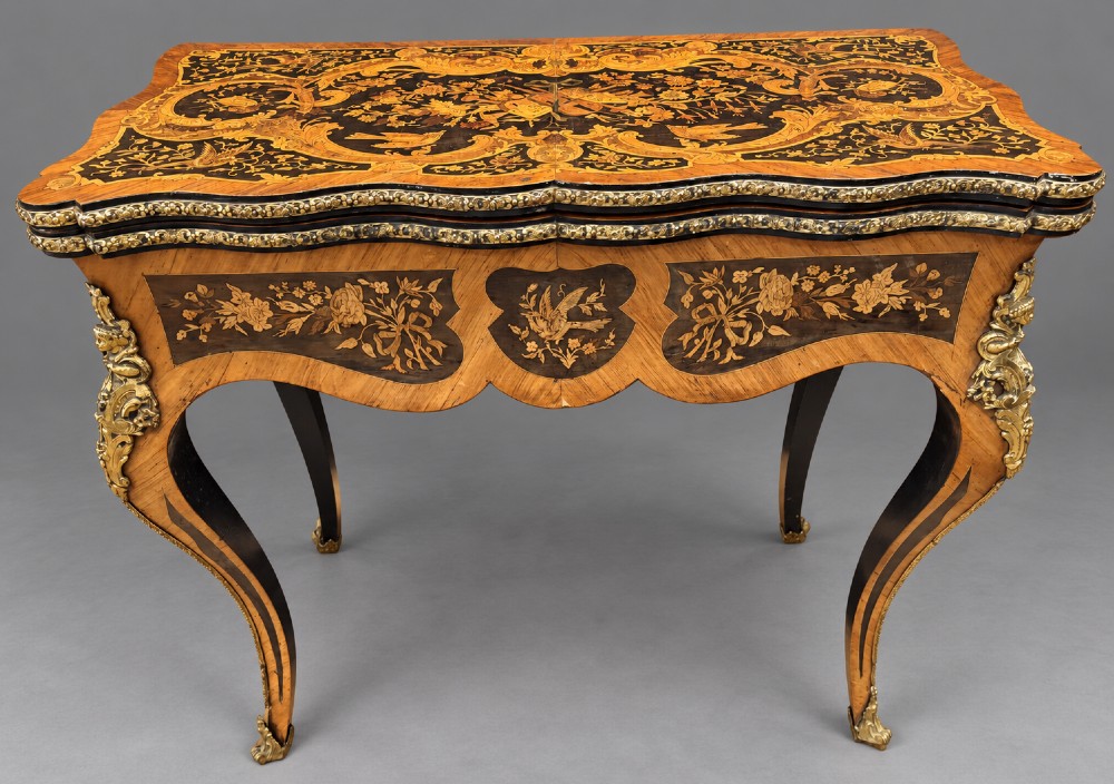 A French Rococo Revival marquetry games table featuring elaborate floral and bird inlay, cast brass mounts, and cabriole legs.