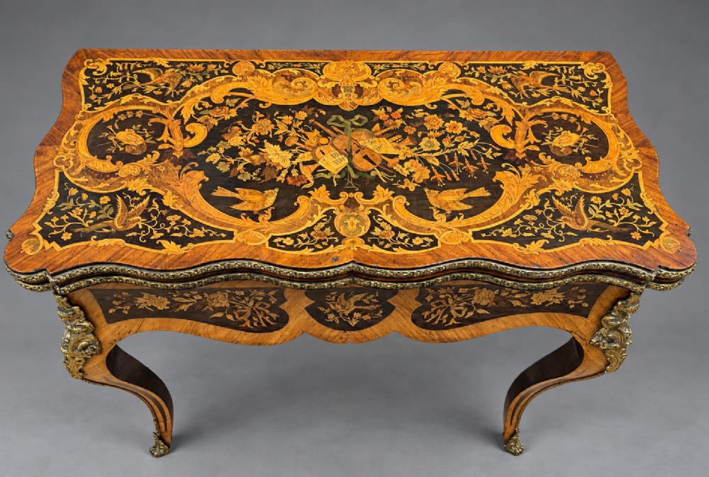 A French Rococo Revival marquetry games table featuring elaborate floral and bird inlay, cast brass mounts, and cabriole legs. View II
