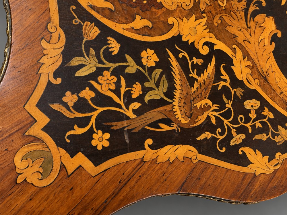 A French Rococo Revival marquetry games table featuring elaborate floral and bird inlay, cast brass mounts, and cabriole legs. View V