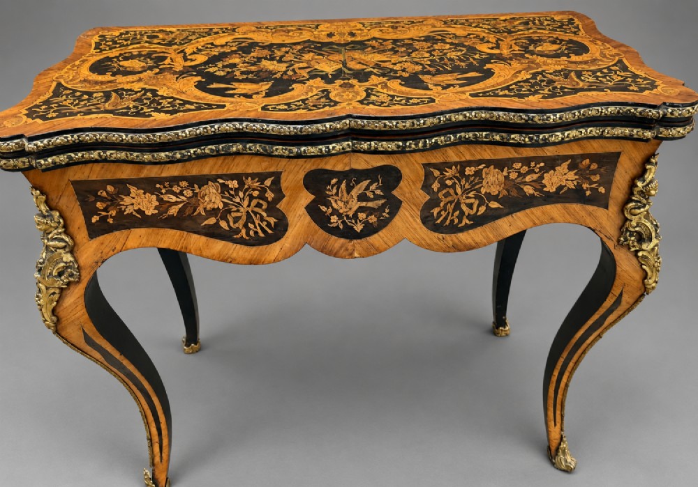 A French Rococo Revival marquetry games table featuring elaborate floral and bird inlay, cast brass mounts, and cabriole legs. View XI