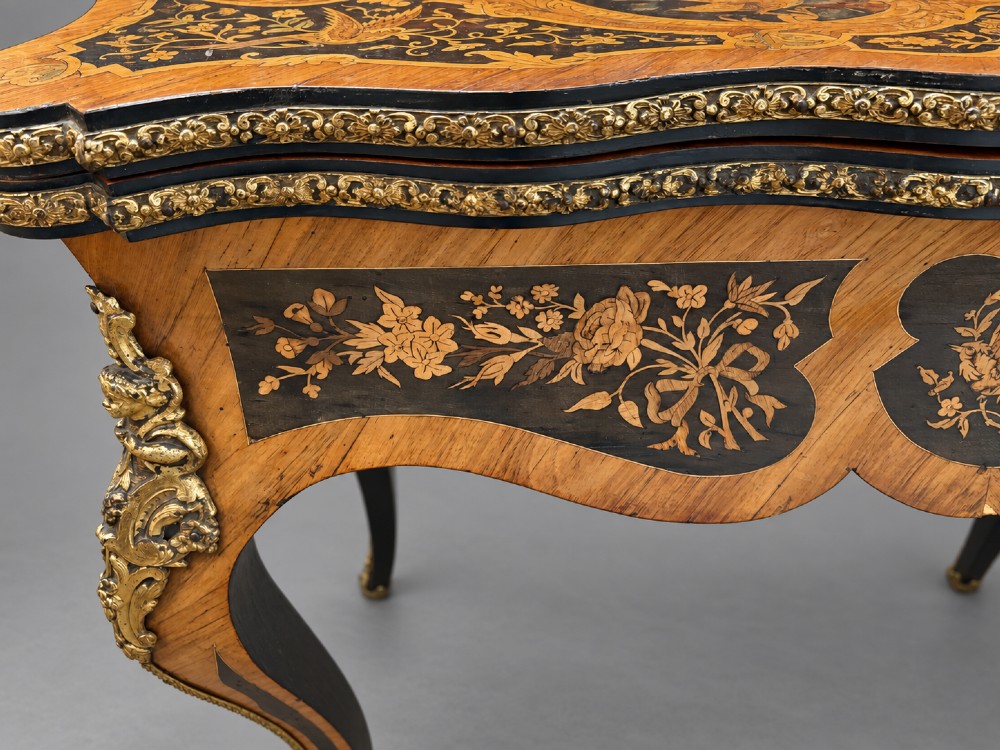 A French Rococo Revival marquetry games table featuring elaborate floral and bird inlay, cast brass mounts, and cabriole legs. View XIII