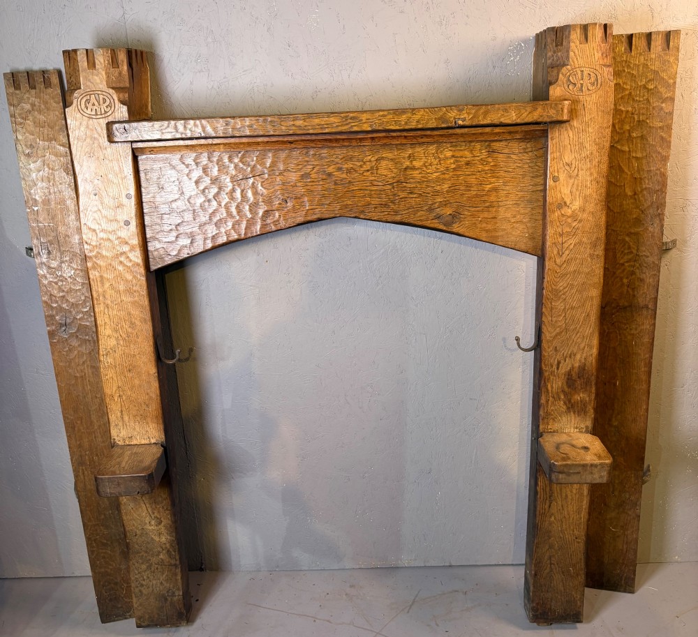 A hand-carved solid oak fire surround featuring an adzed finish, castellated top posts, carved monograms, and small side shelves.