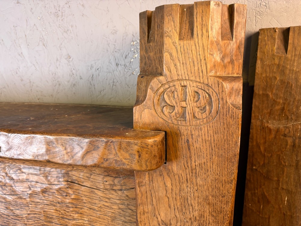 A hand-carved solid oak fire surround featuring an adzed finish, castellated top posts, carved monograms, and small side shelves. View III