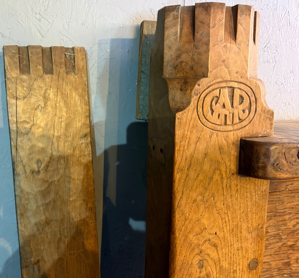 A hand-carved solid oak fire surround featuring an adzed finish, castellated top posts, carved monograms, and small side shelves. View VII