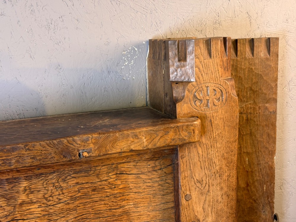 A hand-carved solid oak fire surround featuring an adzed finish, castellated top posts, carved monograms, and small side shelves. View IX