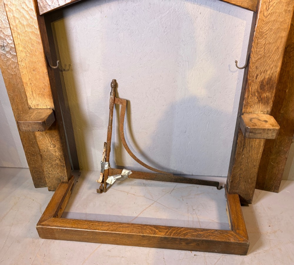 A hand-carved solid oak fire surround featuring an adzed finish, castellated top posts, carved monograms, and small side shelves. View X