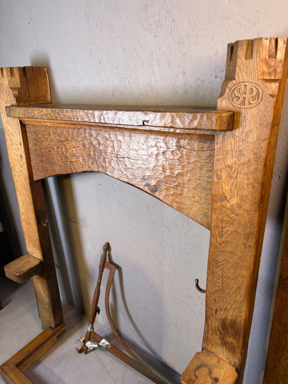 A hand-carved solid oak fire surround featuring an adzed finish, castellated top posts, carved monograms, and small side shelves. View XII