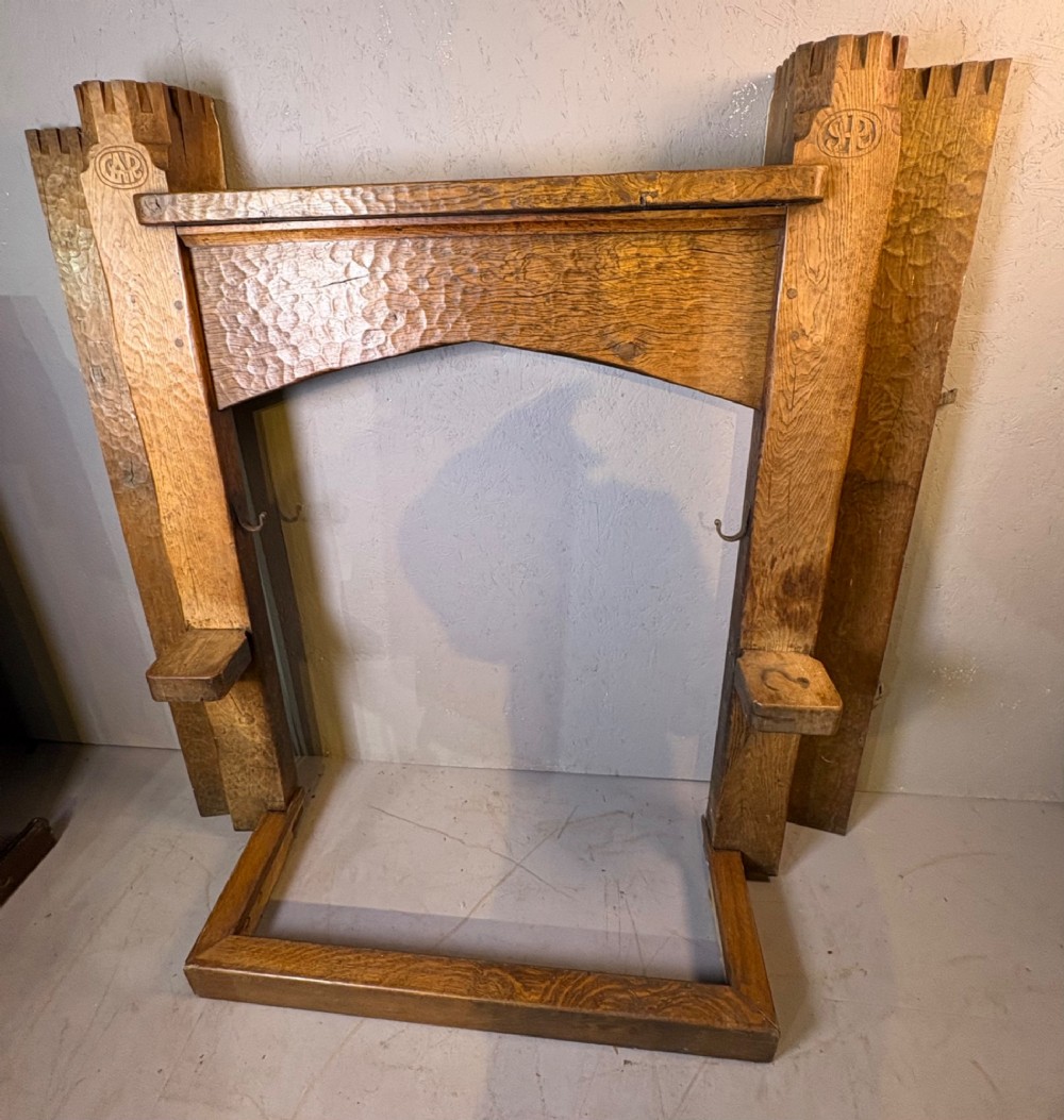 A hand-carved solid oak fire surround featuring an adzed finish, castellated top posts, carved monograms, and small side shelves. View XV