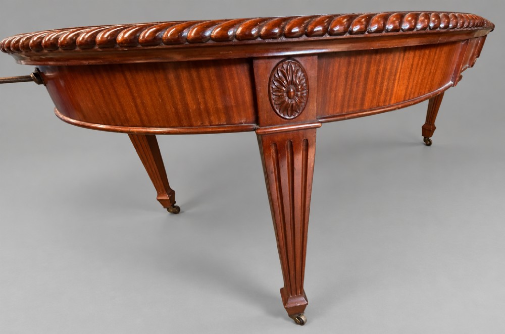 An oval mahogany extending dining table with a carved edge and winding mechanism, surrounded by eight carved wooden chairs featuring blue floral needlepoint seats. View V