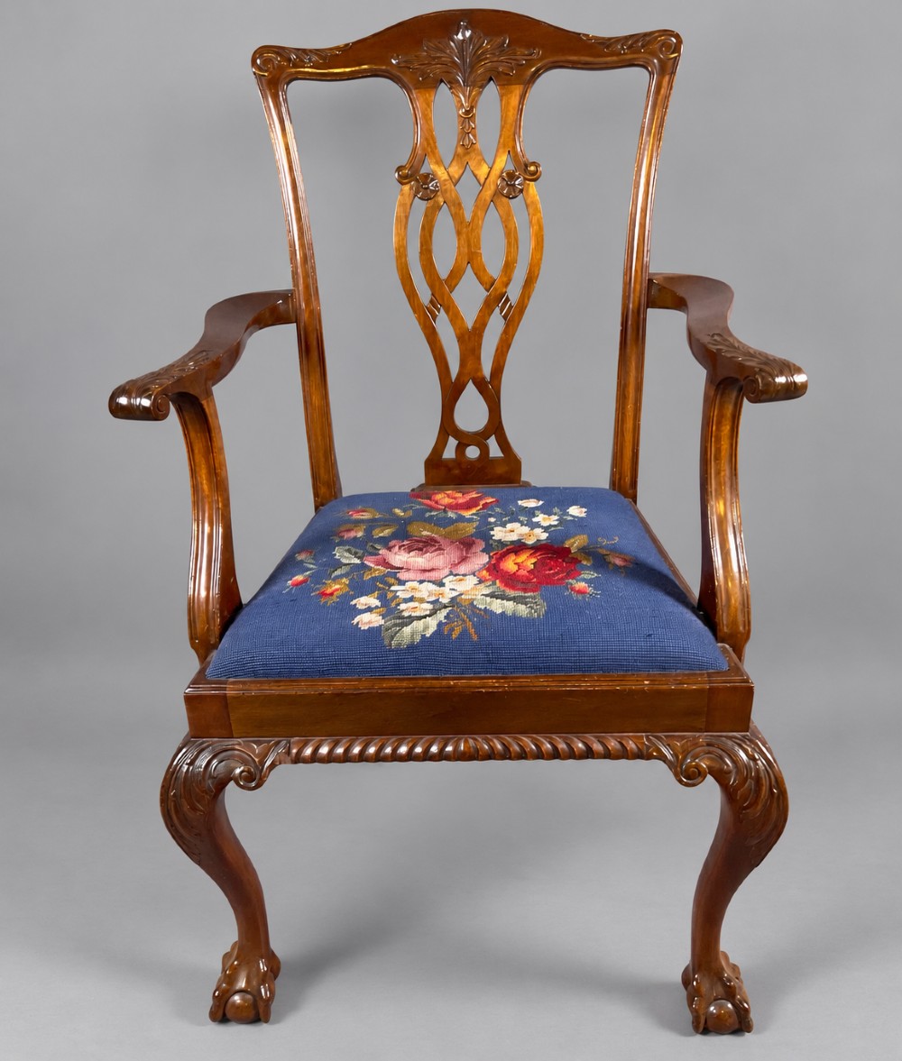 An oval mahogany extending dining table with a carved edge and winding mechanism, surrounded by eight carved wooden chairs featuring blue floral needlepoint seats. View IX