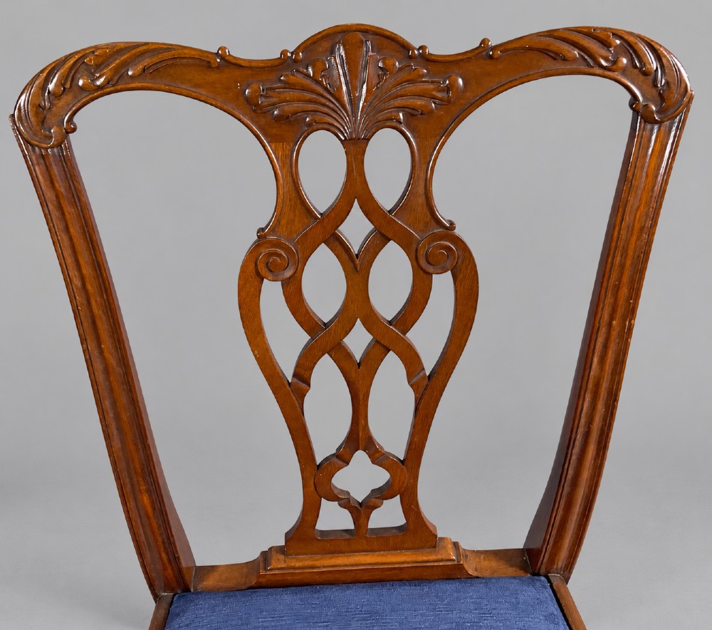 An oval mahogany extending dining table with a carved edge and winding mechanism, surrounded by eight carved wooden chairs featuring blue floral needlepoint seats. View XIII