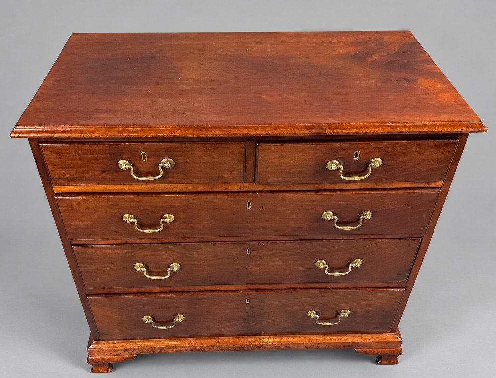 A Georgian mahogany chest of drawers featuring two short drawers over three long graduated drawers with brass swan-neck handles and bracket feet. View IV