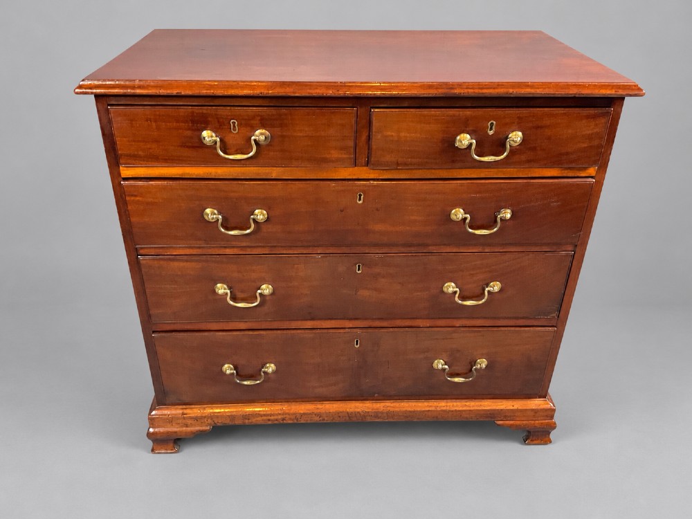 A Georgian mahogany chest of drawers featuring two short drawers over three long graduated drawers with brass swan-neck handles and bracket feet. View V