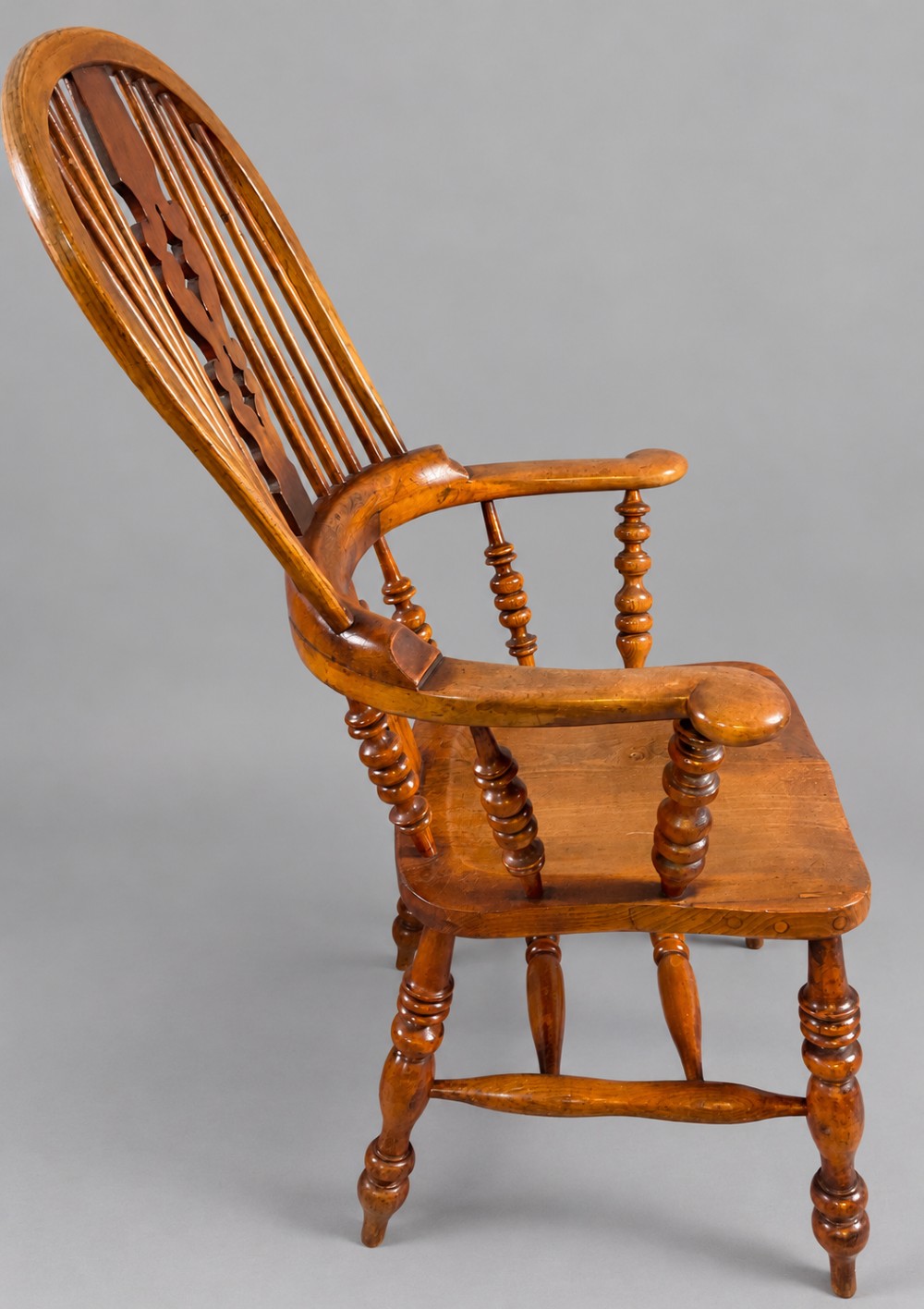 An antique Victorian wooden Windsor armchair featuring a hoop back, a central pierced splat, broad curved armrests, a shaped saddle seat, and turned legs. View II