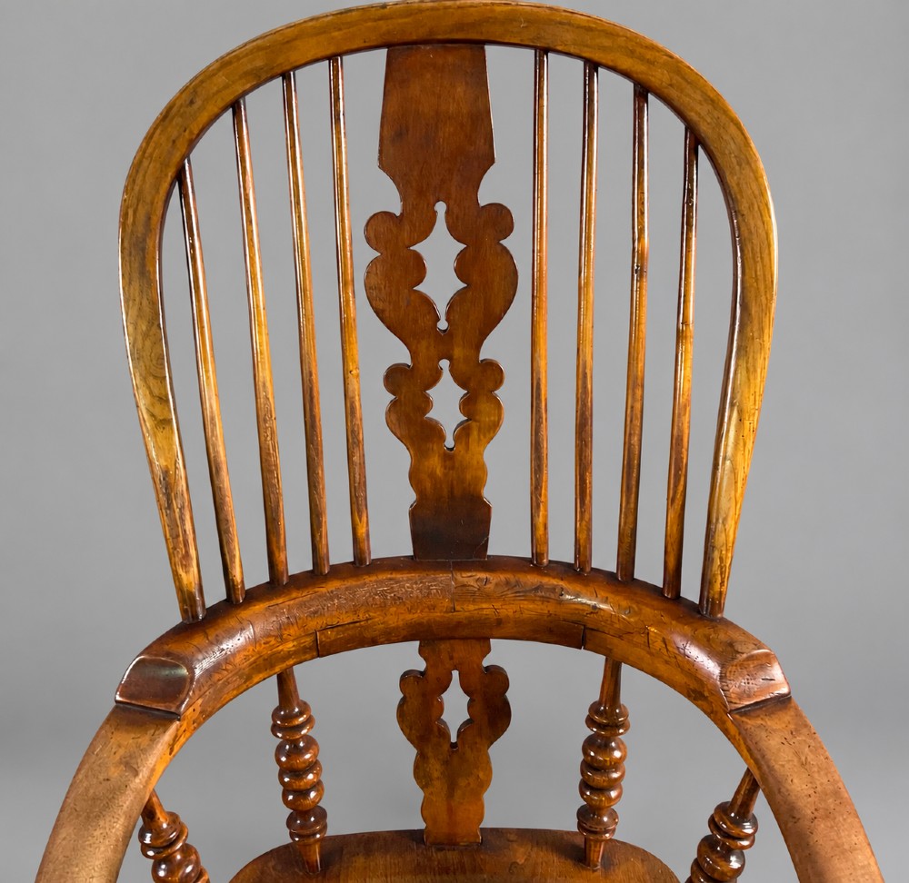 An antique Victorian wooden Windsor armchair featuring a hoop back, a central pierced splat, broad curved armrests, a shaped saddle seat, and turned legs. View III