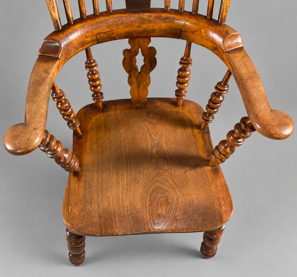 An antique Victorian wooden Windsor armchair featuring a hoop back, a central pierced splat, broad curved armrests, a shaped saddle seat, and turned legs. View V