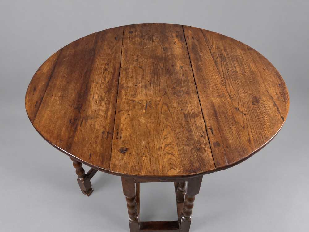A 17th-century oak gateleg dining table with an oval drop-leaf top, turned legs, a box stretcher base, and a small end drawer. View II