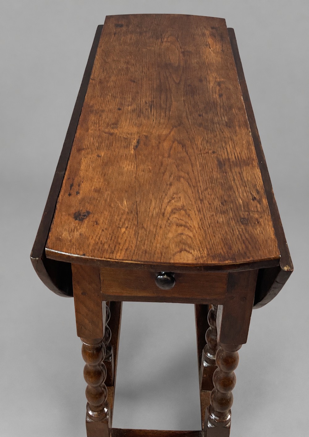 A 17th-century oak gateleg dining table with an oval drop-leaf top, turned legs, a box stretcher base, and a small end drawer. View III