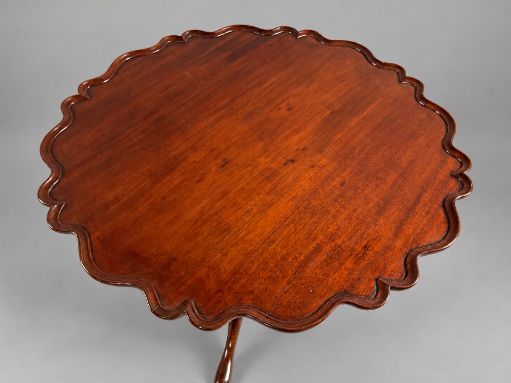 An 18th-century mahogany tilt-top supper table positioned vertically, displaying a scalloped piecrust edge rim and a turned tripod base with carved cabriole legs. View III