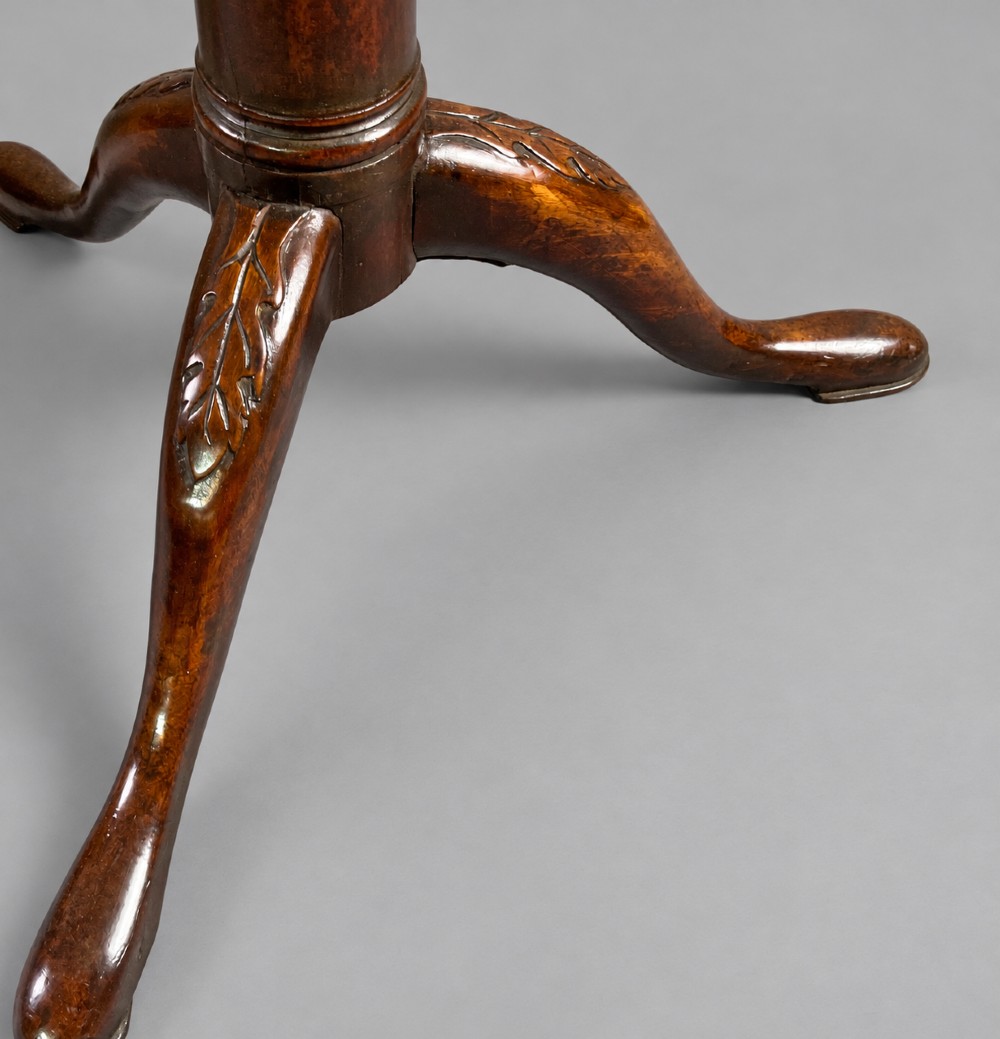 An 18th-century mahogany tilt-top supper table positioned vertically, displaying a scalloped piecrust edge rim and a turned tripod base with carved cabriole legs. View VII