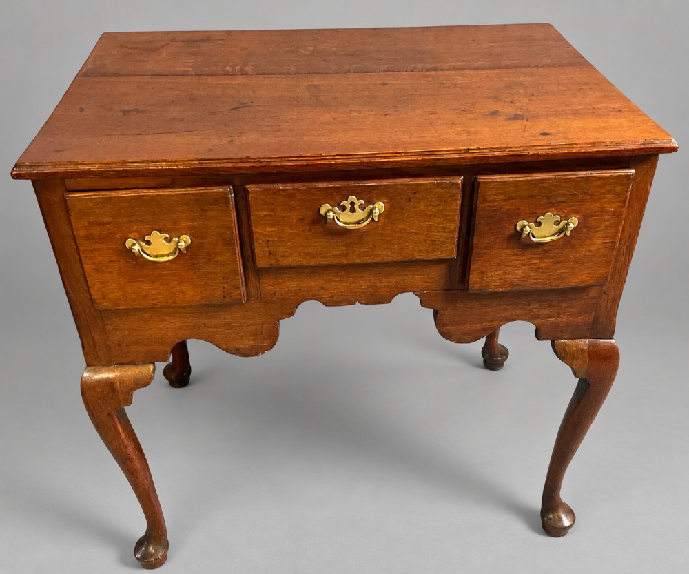 A Georgian oak lowboy featuring three drawers with brass handles, a shaped apron, and cabriole legs ending in pad feet.