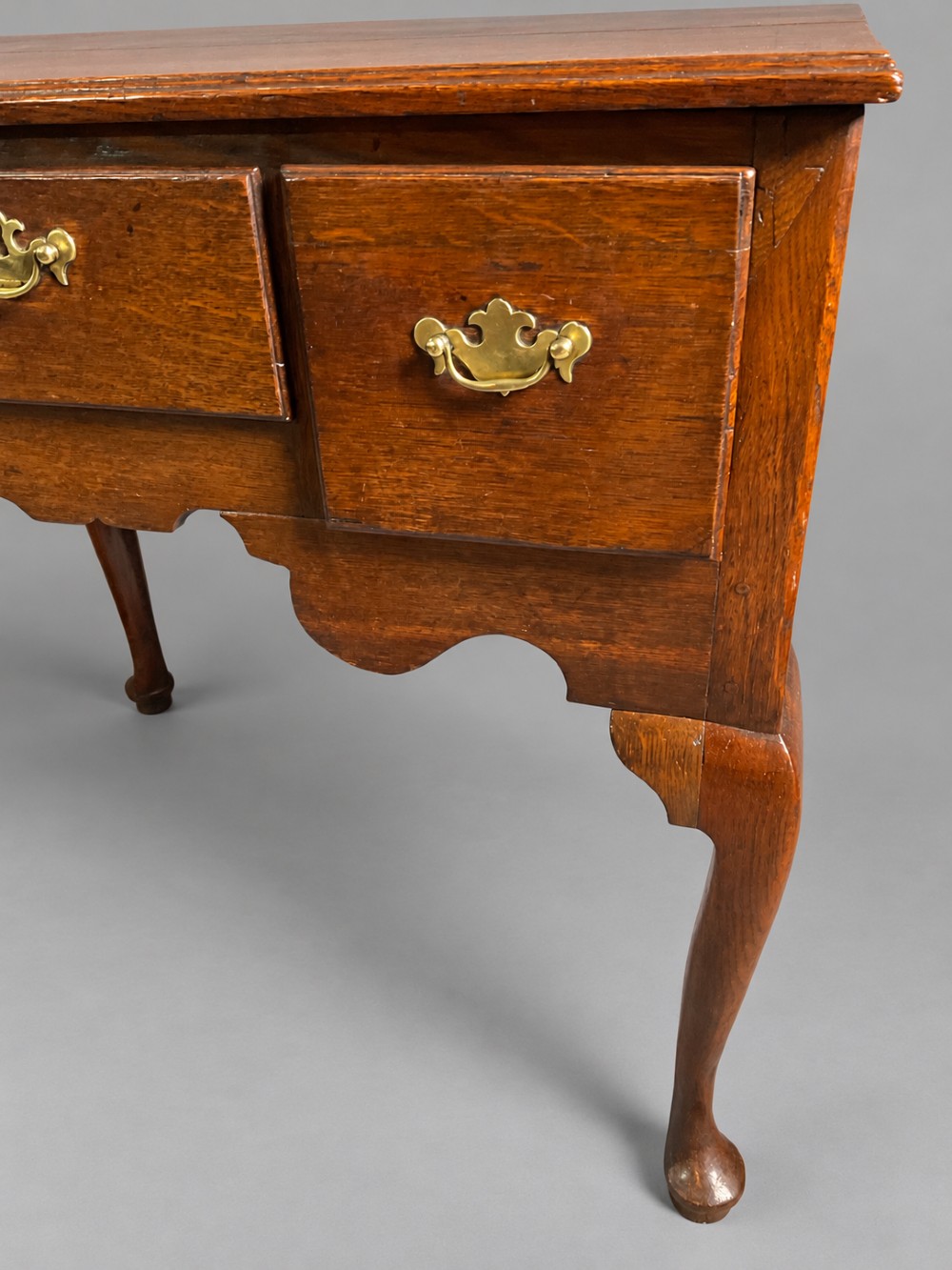 A Georgian oak lowboy featuring three drawers with brass handles, a shaped apron, and cabriole legs ending in pad feet. View IV